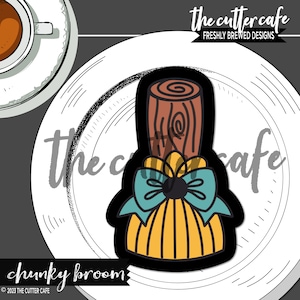 May include: A yellow and brown chunky broom cookie cutter with a blue bow. The cookie cutter is on a white plate with a black and white pattern.