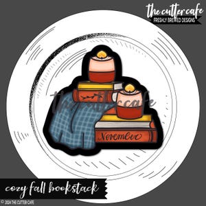 May include: A stack of books with a blue plaid blanket and two red candles on top. The top book has the word "November" written on it.