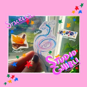May include: A set of Studio Ghibli stickers featuring a white dragon with blue accents, a campfire, and soot sprites. The stickers are on a clear background with a pink border and colourful stars.