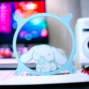 May include: A light blue and white decorative frame featuring a cartoon dog character. The frame has a circular design with a dog figure in the centre. The dog has large ears and is in a seated position.