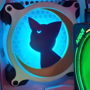 May include: A computer fan featuring a black cat silhouette within a gold crescent moon, illuminated by a blue light. The fan has a white and black frame, with a honeycomb pattern. The AMD logo is visible on the right.