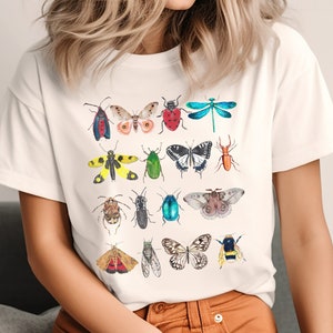 May include: White t-shirt with a colorful insect print. The print features butterflies, beetles, dragonflies, and moths in various colors and patterns.