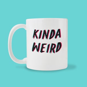 May include: White ceramic mug with black text that reads "Kinda Weird" in a stylized font with a pink and blue glitch effect.
