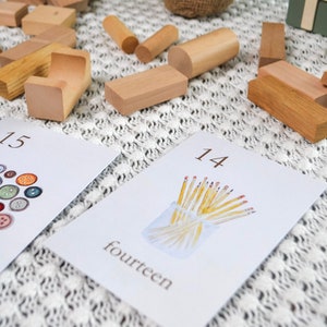 Puede incluir: Dos tarjetas blancas con n&uacute;meros y palabras en ellas. La tarjeta de la izquierda muestra el n&uacute;mero 15 y la palabra "quince" y tiene una imagen de 15 botones de diferentes colores. La tarjeta de la derecha muestra el n&uacute;mero 14 y la palabra "catorce" y tiene una imagen de 14 l&aacute;pices amarillos en un frasco de vidrio.