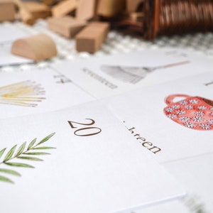 Puede incluir: Un conjunto de tarjetas blancas con ilustraciones y n&uacute;meros. Las tarjetas presentan una variedad de im&aacute;genes, incluyendo una taza de caf&eacute;, una escoba, un manojo de trigo y una rama de hojas verdes. Los n&uacute;meros en las tarjetas van del 13 al 20.