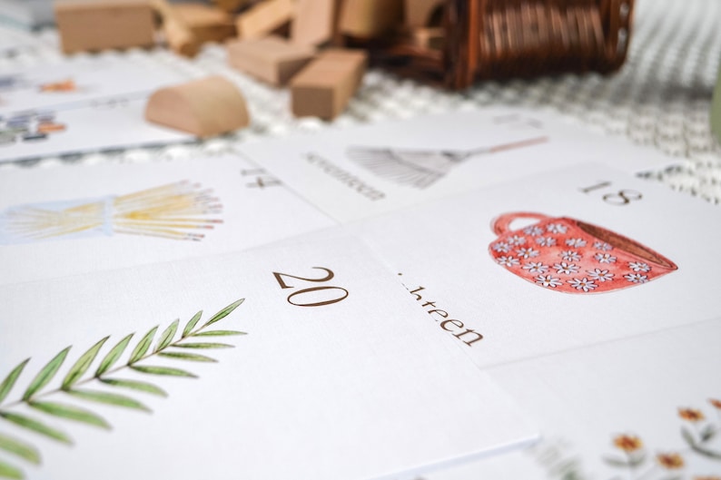 Puede incluir: Un conjunto de tarjetas blancas con ilustraciones y n&uacute;meros. Las tarjetas presentan una variedad de im&aacute;genes, incluyendo una taza de caf&eacute;, una escoba, un manojo de trigo y una rama de hojas verdes. Los n&uacute;meros en las tarjetas van del 13 al 20.