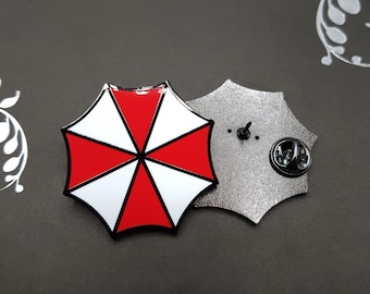 May include: A red and white umbrella pin with a black outline. The back of the pin is silver and has a pin back.
