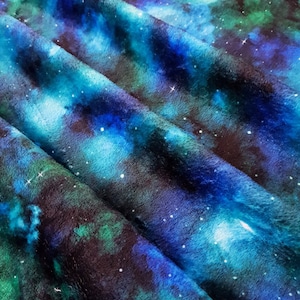 May include: A soft, blue, green and black fabric with a galaxy print. The fabric is folded and has a fuzzy texture.