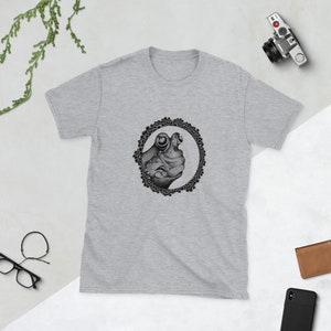 May include: A grey t-shirt with a black and white illustration of a frog's face inside a circle of dots.