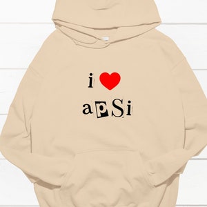 Peut inclure: Un sweat à capuche beige avec un cœur rouge et le texte "i ♥ a pSi" imprimé sur le devant.