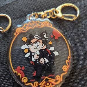 Op de afbeelding: Een heldere acryl sleutelhanger met een stripfiguur in een zwart pak, witte vlinderdas en kattenoren. Het personage bevindt zich in een decoratief goudkleurig frame. De sleutelhanger heeft een goudkleurige sluiting.