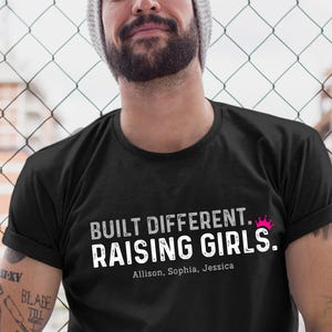 May include: Black t-shirt with white text that reads "BUILT DIFFERENT. RAISING GIRLS." A pink crown graphic is above the word "GIRLS." The names Allison, Sophia, and Jessica are below the text.