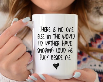 May include: White ceramic mug with a black heart and the text "THERE IS NO ONE ELSE IN THE WORLD I'D RATHER HAVE SNORING LOUD AS FUCK BESIDE ME". The mug has a white handle.