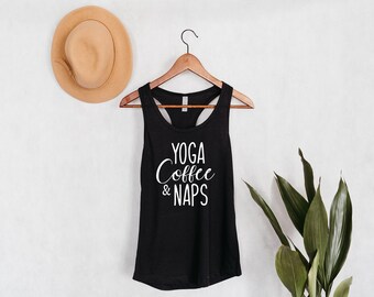 Può includere: Canotta nera con la scritta "Yoga Coffee & Naps" in lettere bianche. La canotta è appesa a un appendiabiti di legno su uno sfondo bianco.