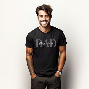 May include: Black t-shirt with the word "DAD" in large, gray letters. The names "ethan" and "liam" are written in smaller, gray letters below the word "DAD".
