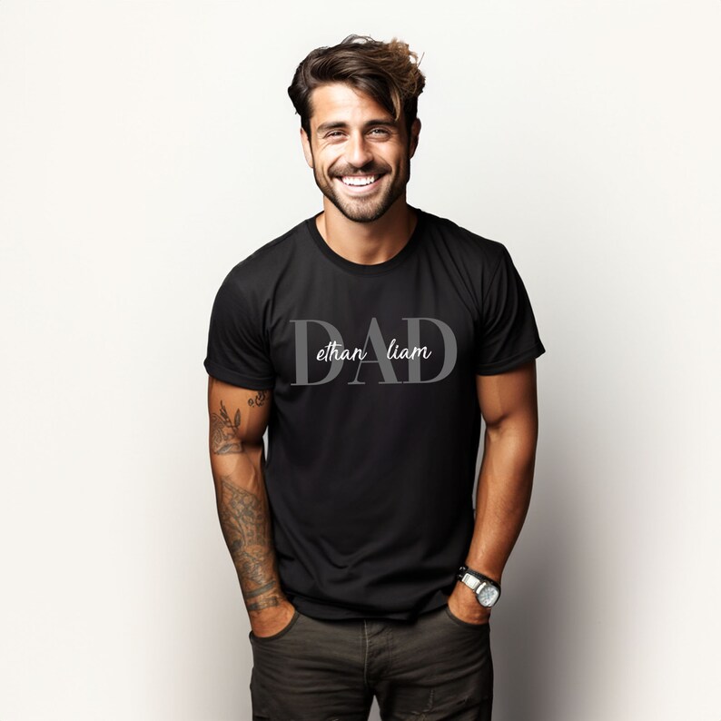 May include: Black t-shirt with the word "DAD" in large, gray letters. The names "ethan" and "liam" are written in smaller, gray letters below the word "DAD".