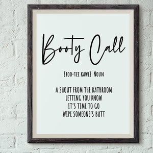 May include: Framed wall art with the words "Booty Call" in a black script font. The definition is below, with the pronunciation, and the phrase "A shout from the bathroom letting you know it's time to go wipe someone's butt."