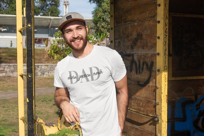 May include: A white t-shirt with the word "DAD" printed in gray with the names "olivia, jessica, noah" printed underneath.