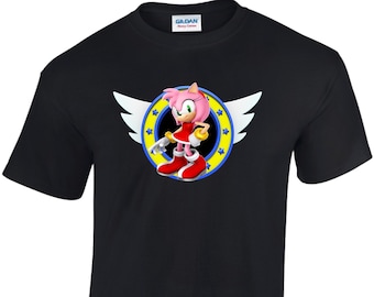 May include: Black t-shirt with a graphic of Amy Rose from the Sonic the Hedgehog video game series. The graphic features Amy Rose standing in front of a yellow ring with blue stars and white wings.