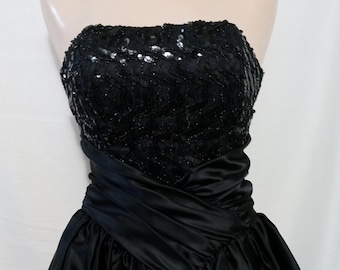 May include: A black strapless dress with a sequined bodice and a satin skirt. The skirt has a ruffled hem and a layered design.
