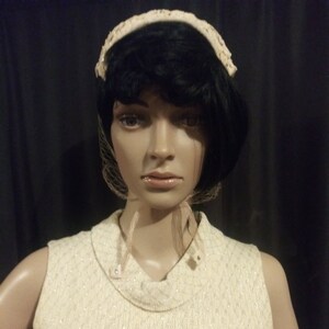 May include: A white knitted sleeveless top with a high neckline and a subtle sparkle. The top is worn by a mannequin with a black wig and a white lace headband.