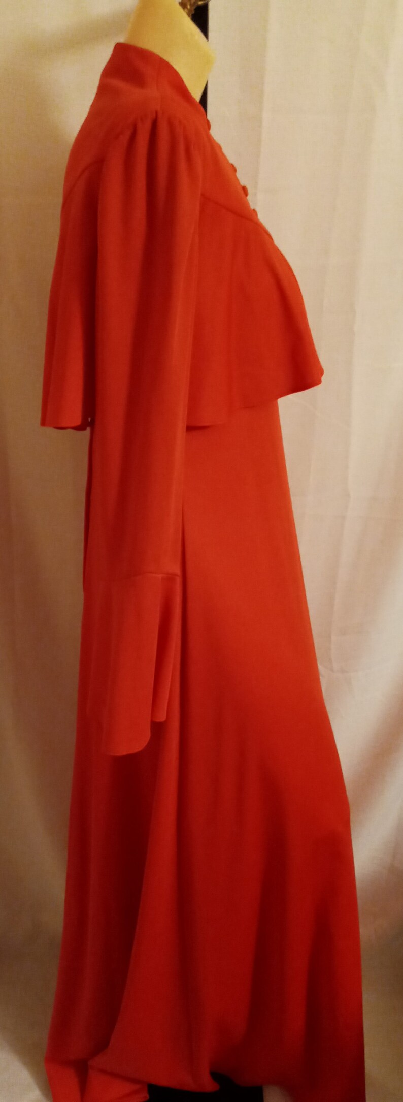 May include: A long, red dress with a ruffled collar and long sleeves. The dress has a fitted bodice and a flowing skirt.