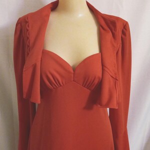 May include: A long, rust-colored dress with a matching jacket. The dress has a sweetheart neckline and long bell sleeves. The jacket has a ruffled collar and long sleeves.
