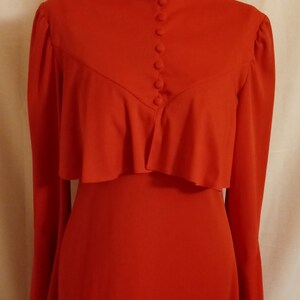May include: A long-sleeved, red dress with a ruffled neckline and a row of buttons down the front.