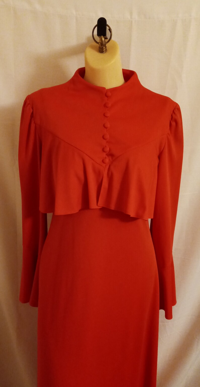 May include: A long-sleeved, red dress with a ruffled neckline and a row of buttons down the front.
