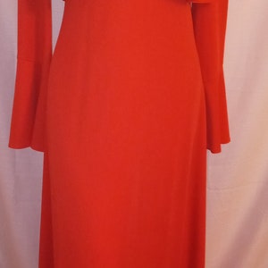 May include: A long red dress with a high neckline and a ruffled collar. The dress has a keyhole opening at the neckline and is fastened with buttons. The dress has long sleeves with bell bottoms.