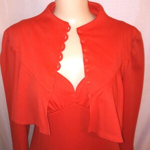 May include: A bright orange dress with a high collar and long sleeves. The dress has a scalloped neckline and a row of buttons down the front.