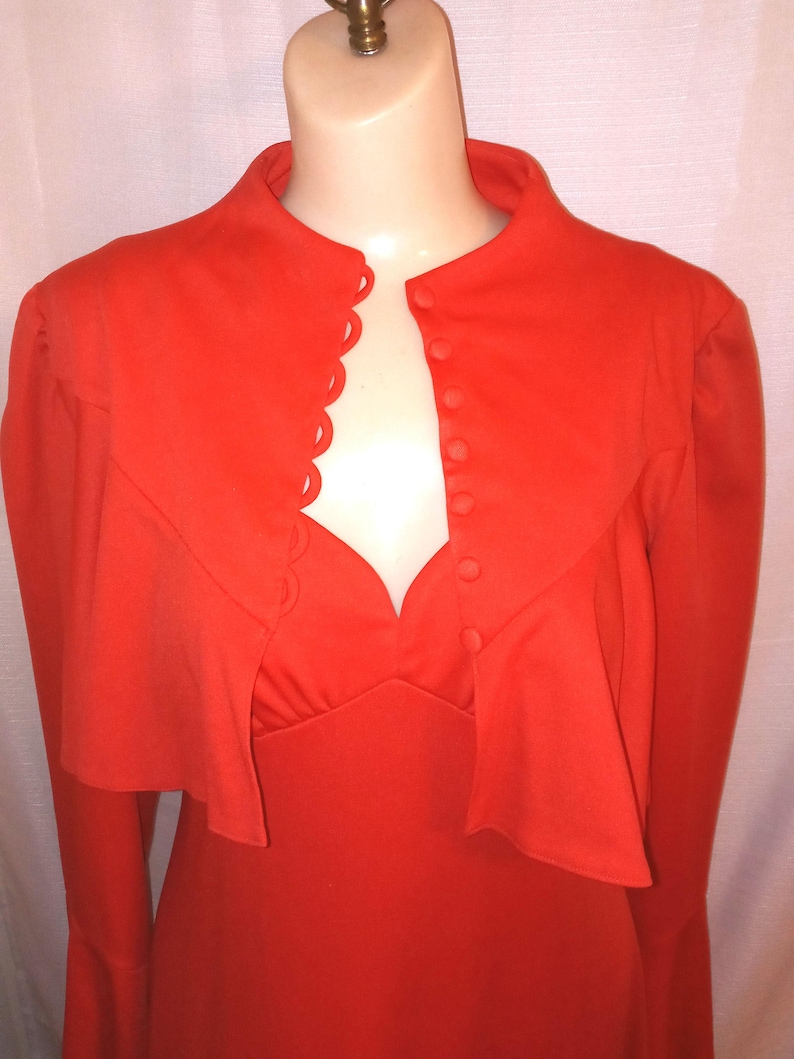 May include: A bright orange dress with a high collar and long sleeves. The dress has a scalloped neckline and a row of buttons down the front.