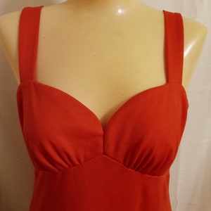 May include: A red sleeveless dress with a sweetheart neckline. The dress is made of a smooth, silky fabric.