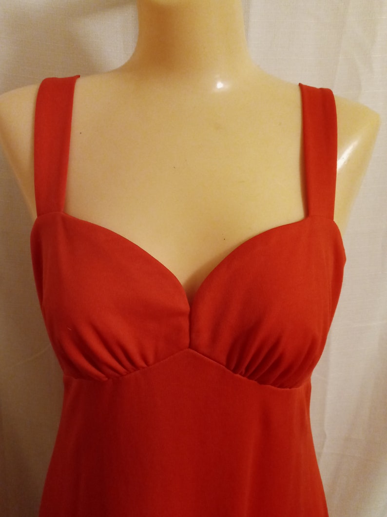 May include: A red sleeveless dress with a sweetheart neckline. The dress is made of a smooth, silky fabric.