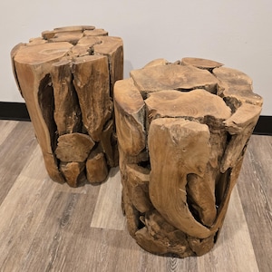 May include: Two natural wood side tables. Each table is cylindrical, constructed from irregularly shaped pieces of wood, creating a rustic, textured surface. The tables are a warm brown color and sit on a light-colored wood floor.