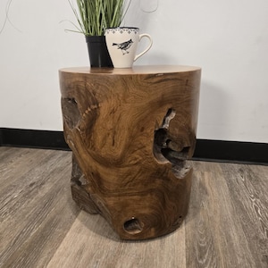 May include: A cylindrical side table crafted from a solid piece of natural brown wood with a smooth top surface and a textured, organic exterior featuring deep knots and crevices. A white ceramic mug with a bird illustration sits on top.