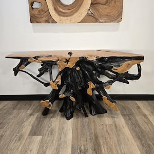 May include: A natural wood console table with a live edge top and a black root base. The table is made of light brown wood with dark brown and black accents. A matching wood art piece hangs on the wall above the table.