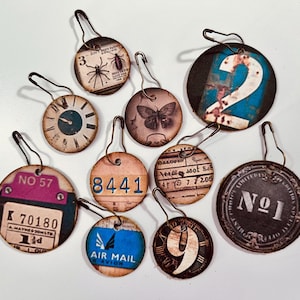 May include: Nine round paper tags with different designs and numbers. The tags are attached to metal rings. The designs include a clock, a butterfly, a spider, a number 2, a number 9, a number 1, a number 57, a number 8441, and a tag that says "Air Mail".