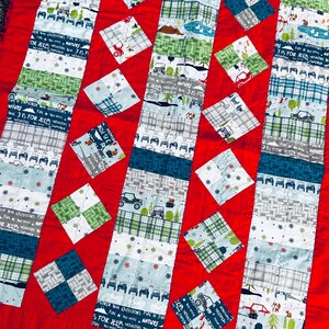 May include: A patchwork quilt with a red background. The quilt features vertical strips and square patches in various patterns, including cars, trees, and plaid. The text "IS FOR JEEP" and "EXPLORER" is visible on some strips. The quilt is a mix of blue, green, and white.