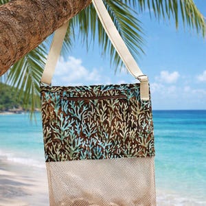 May include: A rectangular crossbody bag featuring a brown fabric upper section with a light blue and teal coral reef pattern, a horizontal zippered pocket, and a lower section made of beige mesh fabric, suspended by an adjustable cream strap.