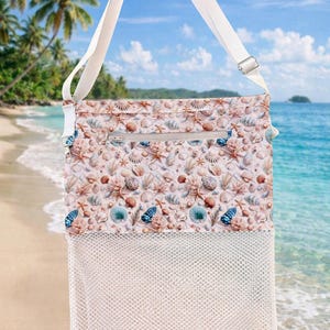May include: A rectangular crossbody bag featuring a white adjustable strap and a top zipper closure. The upper section displays a repeating pattern of seashells and starfish in shades of pink, blue, and tan, while the lower section is white mesh.