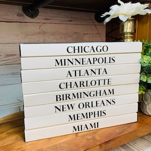 May include: White wooden sign with black text listing the names of cities: Chicago, Minneapolis, Atlanta, Charlotte, Birmingham, New Orleans, Memphis, Miami.