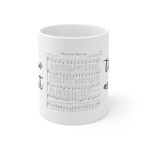 May include: A white ceramic mug featuring the printed musical score and lyrics for the hymn How Great Thou Art. The text is displayed in black ink against the white background, with the title How Great Thou Art clearly visible at the top.