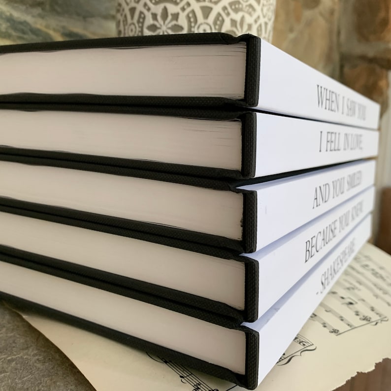 May include: A stack of five white books with black spines. The books have text on the spines that reads "When I Saw You", "I Fell In Love", "And You Smiled", "Because You Are", "Shakespeare".