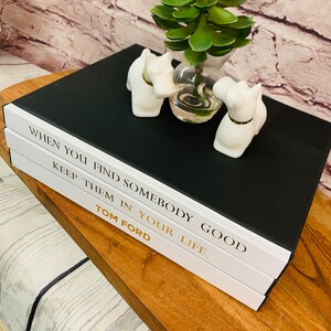 May include: Three black and white hardcover books stacked on top of each other. The top book has the text "WHEN YOU FIND SOMEBODY GOOD KEEP THEM IN YOUR LIFE." The bottom book has the text "TOM FORD".