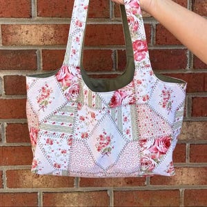 May include: A patchwork tote bag with a floral pattern. The bag features a variety of fabric squares in shades of white, pink, and green, with a repeating rose design. The handles and interior lining are a solid green color.