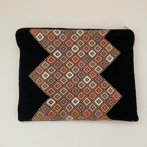 May include: Black zippered pouch with a geometric pattern in shades of pink, brown, and white.