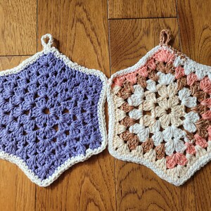 May include: Two crocheted star-shaped pot holders. One is purple with a white border, the other is multi-colored with brown, white, and pink yarn.