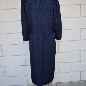 May include: A navy blue dress with a long sleeve and a swirling pattern. The dress has a cinched waist and a midi length.
