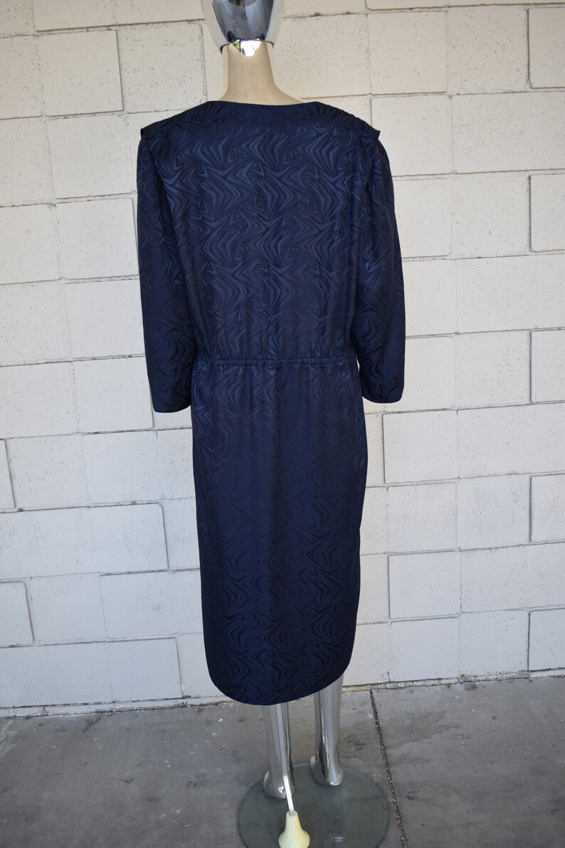 May include: A navy blue dress with a long sleeve and a swirling pattern. The dress has a cinched waist and a midi length.